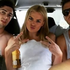 three people sitting in the back of a car and one person holding up two fingers