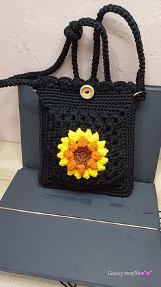 a black crocheted bag with a yellow flower on the front and side, sitting on top of a table