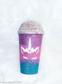 a purple and blue glitter cup with a unicorn face on the lid, sitting on a white fur surface