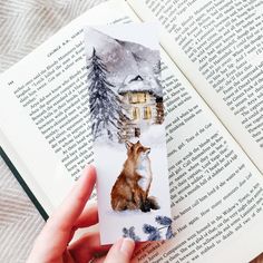 a person holding an open book with a picture of a fox on it and a house in the background