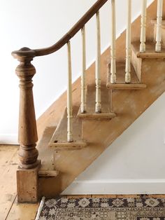 an old wooden stair case next to a rug on the floor in front of a white wall