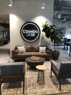 an office lobby with couches, chairs and tables in front of a common desk sign