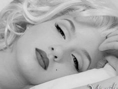 a black and white photo of a blonde haired woman with her eyes closed, laying on a bed