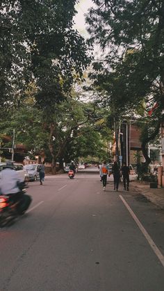 people are riding motorcycles down the street in front of some buildings and trees on either side of the road