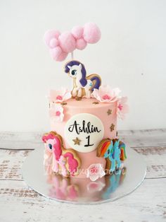 a birthday cake with pink frosting and pom poms on top is decorated with an image of a pony