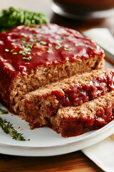 meatloaf with sauce and herbs on a plate next to some broccoli