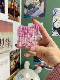 a person holding up a piece of beaded art in front of a wall with pictures on it