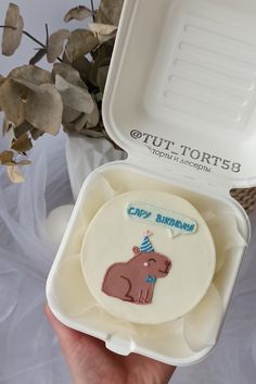 a person holding up a small cake in a box with an elephant design on it