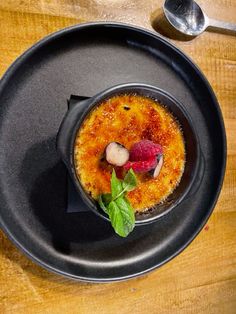 a black plate topped with a dessert on top of a wooden table next to a spoon