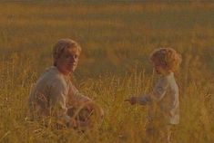 two people sitting in tall grass with one pointing at the other's hand,