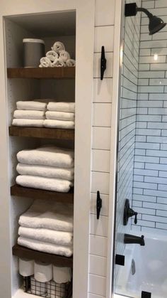 towels are stacked on shelves in the corner of a shower stall, with white subway walls