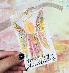 a hand holding up a christmas card with an angel on it and the words merry christmas