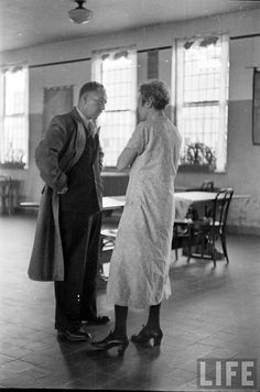 an old black and white photo of two people standing in a large room with windows