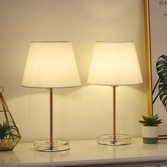 two lamps sitting on top of a white table next to a plant and potted plant