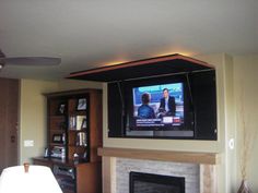 a flat screen tv mounted on the wall above a fireplace in a living room with a ceiling fan