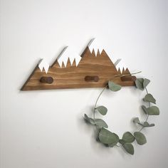 a wooden wall hanging with mountains and leaves on the bottom, along with two knives stuck in it