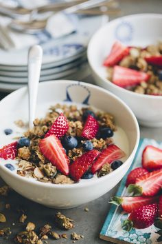 two bowls filled with granola and strawberries on top of a table next to plates