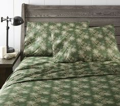 a bed with green sheets and pillows on top of it next to a night stand