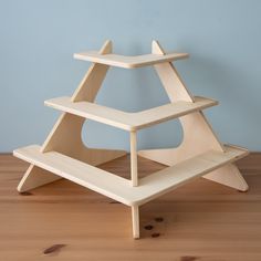 a three tiered wooden shelf sitting on top of a hard wood floor next to a blue wall