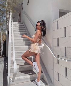 a woman leaning up against the side of a white wall next to some stairs with her hand in her pocket