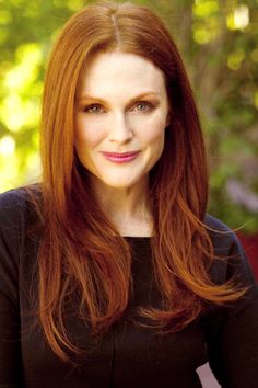 a woman with long red hair wearing a black shirt and purple lipstick looks into the camera