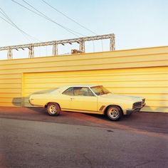 an old car is parked in front of a yellow building with power lines above it