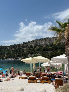 many people are sitting on the beach under umbrellas and lounge chairs near the water