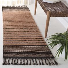 a brown and black rug with tassels next to a plant on a white floor