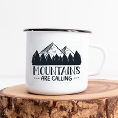 a white coffee mug sitting on top of a tree stump with mountains in the background