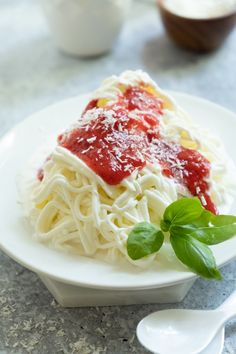 a white plate topped with pasta covered in sauce and garnished with green leaves