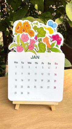 a calendar sitting on top of a wooden table next to a tree and some leaves