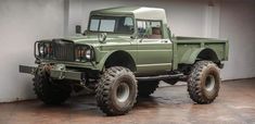 a green truck parked in a garage next to a white wall and cement flooring