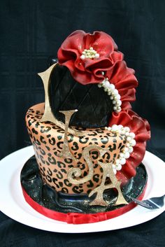 a leopard print cake with red flowers and pearls on top, sitting on a white plate