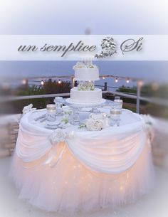 a wedding cake sitting on top of a table covered in white cloths and flowers