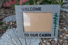 a welcome to our cabin sign in front of some rocks and flowers with the words welcome to our cabin on it