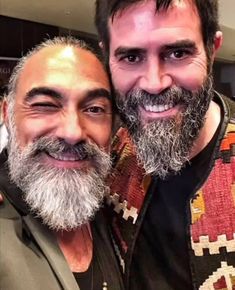 two men with beards are posing for the camera, one is smiling at the camera