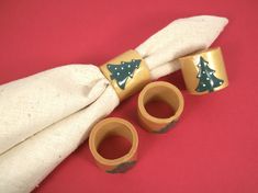 two napkin rings with christmas trees on them sitting next to a white cloth covered napkin