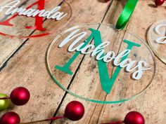 three personalized glass ornaments on top of a wooden table with red and green decorations