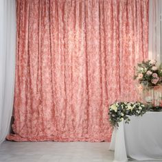 a vase with flowers sitting on top of a table in front of a pink curtain