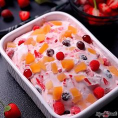 a fruit salad in a white dish with berries and cherries on the table next to it