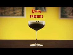 a glass filled with liquid sitting on top of a wooden table next to a yellow wall