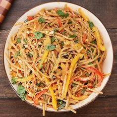 a white bowl filled with noodles and vegetables on top of a wooden table next to chopsticks