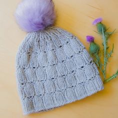 a knitted hat with a purple pom - pom sitting next to it