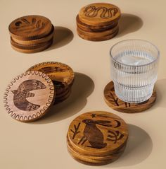 four wooden coasters with designs on them and a glass cup in the middle one