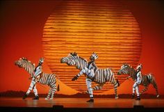 four zebras are standing in front of an orange ball and red background with yellow stripes