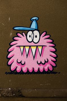 graffiti on the side of a building with a pink monster face wearing a blue hat