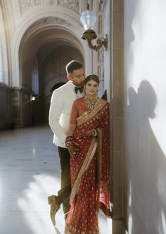 a man and woman standing next to each other in front of a wall with an archway