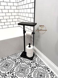 a bathroom with black and white tiles on the floor next to a toilet paper roll