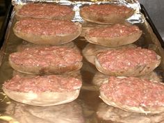 several hamburger patties sitting on top of tin foil covered in sauce and seasoning