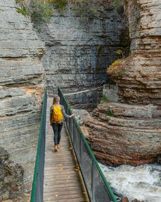 a woman walking across a bridge over a river next to a rocky cliff side area